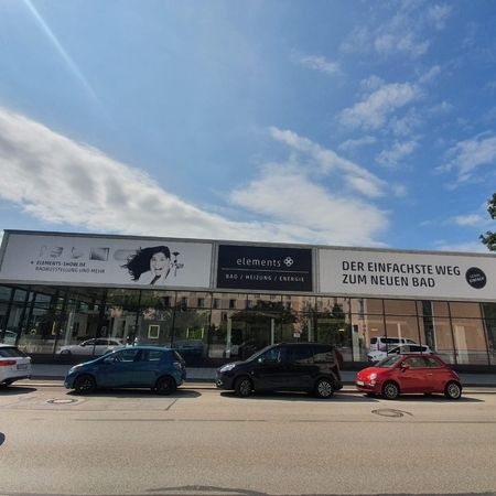 Ausstellungsgebäude mit 'elements'-Schildern und geparkten Autos unter einem blauen Himmel mit Wolken.