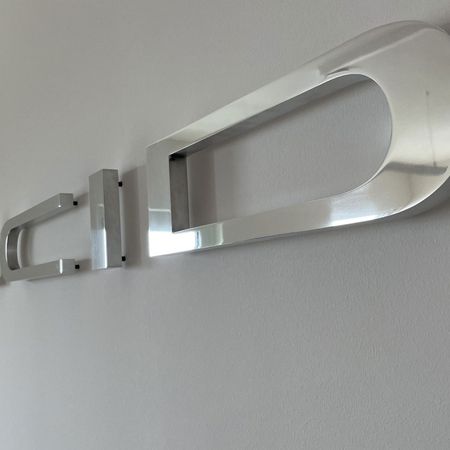 Silberner Wandbuchstabe 'D' mit modernem Design auf weißem Hintergrund.