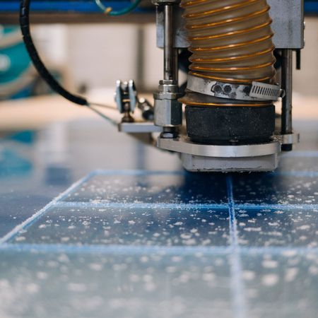 Industrielle Schneidemaschine bei der Arbeit an blauem Material mit verstreuten weißen Abfällen.