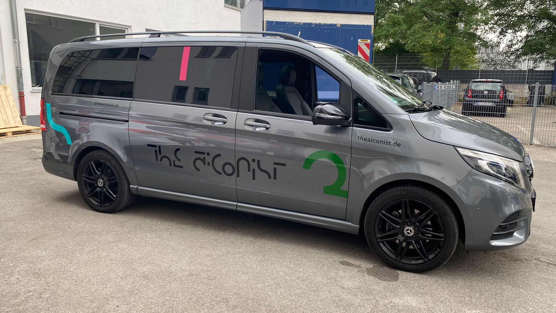 Ein grauer Lieferwagen mit individuellen Grafiken und schwarzen Felgen, der im Freien geparkt ist.