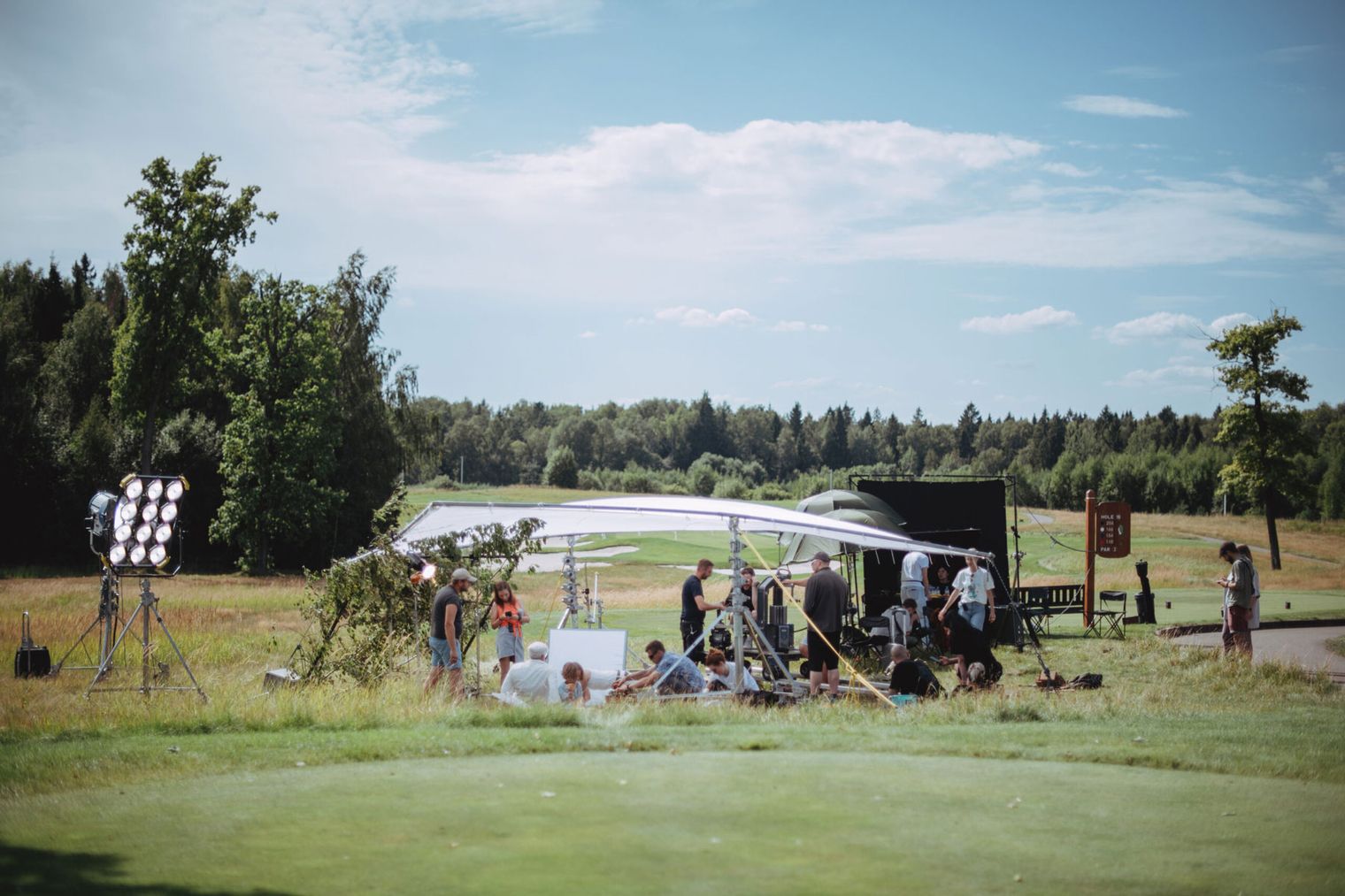 Außenaufnahmen auf einem Golfplatz mit Crew und Ausrüstung unter sonnigem Himmel.