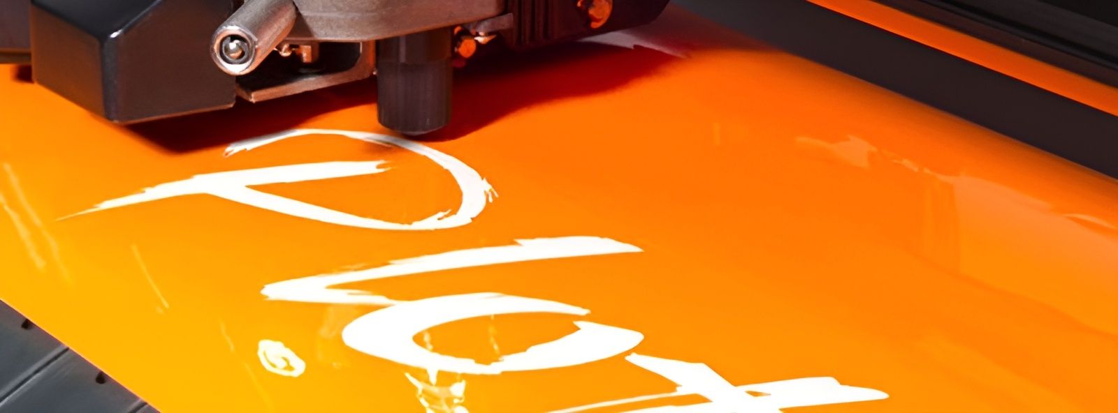 Nahaufnahme einer Plottermaschine, die weißes Vinyl auf orangefarbenem Hintergrund schneidet.