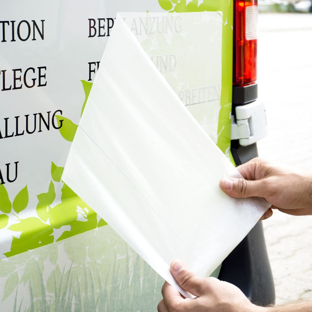 Hände entfernen Klebepapier von einem Schild mit grüner Blattgrafik.