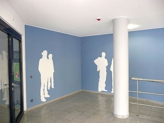 Innenecke mit blauen Wänden mit weißen Silhouetten menschlicher Figuren, einer Säule und Glastüren.