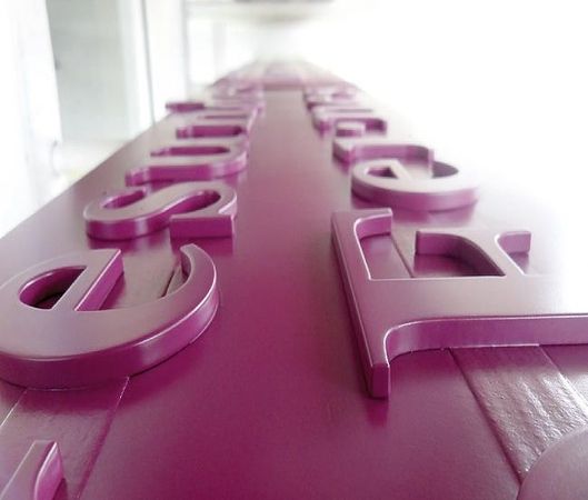 Eine Nahaufnahme von violetten 3D-Buchstaben auf einer passenden Oberfläche, die einen perspektivischen Effekt erzeugt.