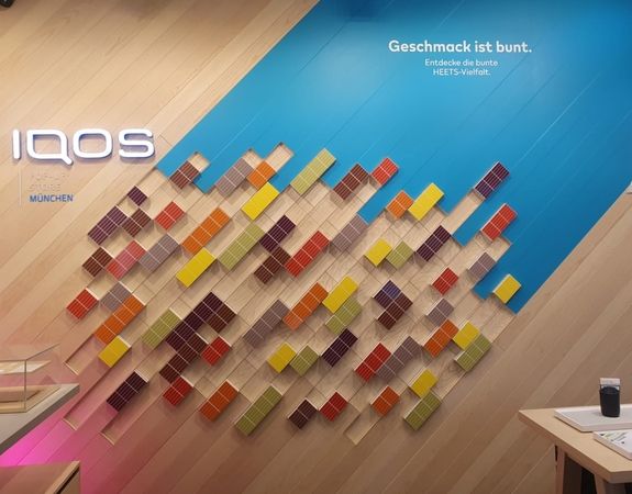 Ein farbenfrohes Wandbild in einem IQOS-Geschäft mit Texttafeln in deutscher Sprache.