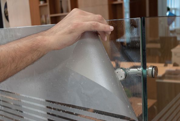 Die Hand einer Person, die in einer Eisenwarenwerkstatt eine durchsichtige Plastikfolie ausrichtet.